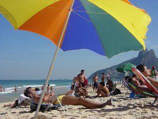 Sunbathers on a beach under a rainbow colored umbrella