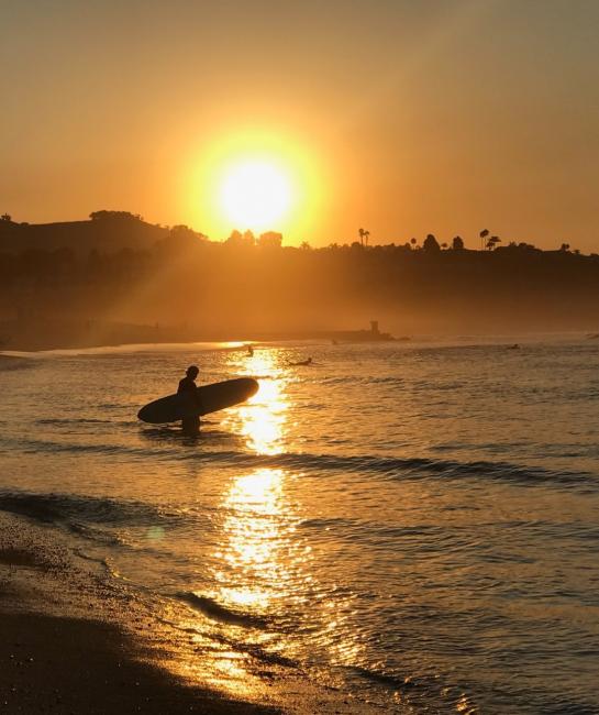 Sun setting behind the hill with silhouetted surfer entering the surf